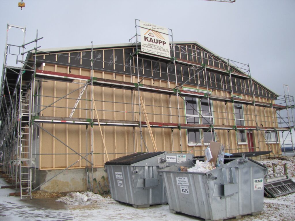 Gebaeude im Bau mit Geruest und Containern im Vordergrund.