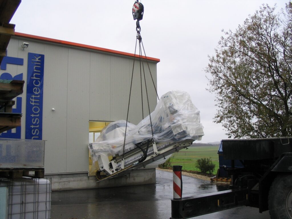 Krangeladener Transport einer großen Maschine vor Bauhalle 2 von Ebert Kunststoffbearbeitung.