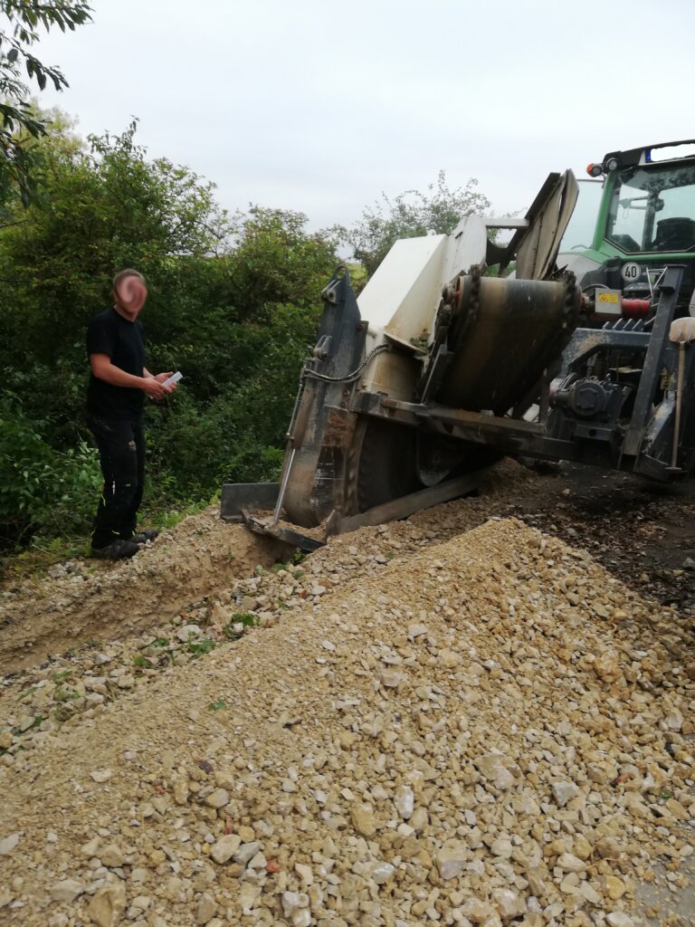 Ein Traktor arbeitet an einer Baustelle, ein Mann steht daneben und ueberwacht die Arbeit.