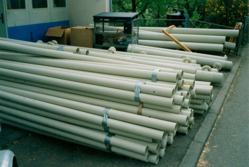 Stapel von Kunststoffrohren vor einem industriellen Gebaeude