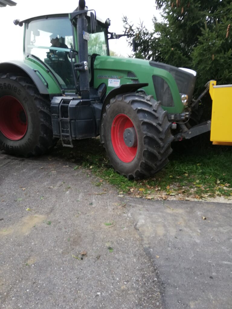 Ein großer gruener Traktor steht auf einem Pflasterweg.